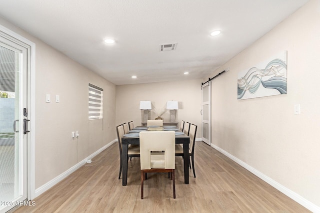 dining space featuring light wood-style flooring, baseboards, a barn door, and visible vents