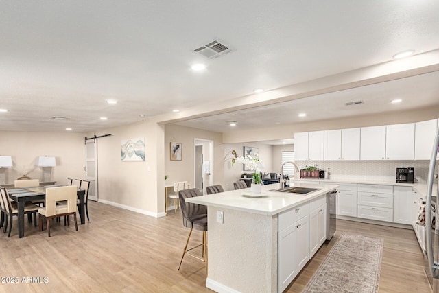 kitchen featuring a sink, a barn door, a breakfast bar, visible vents, and light wood-style floors