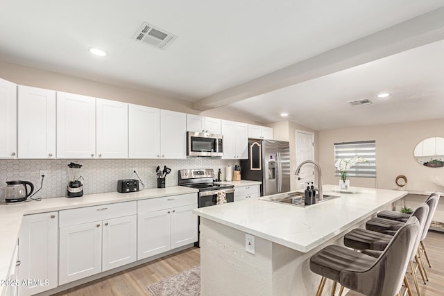 kitchen featuring a kitchen bar, a sink, appliances with stainless steel finishes, and visible vents