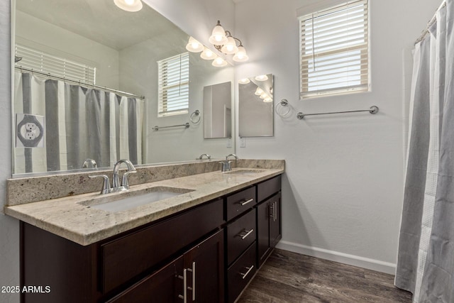 full bathroom with a sink, baseboards, double vanity, and wood finished floors