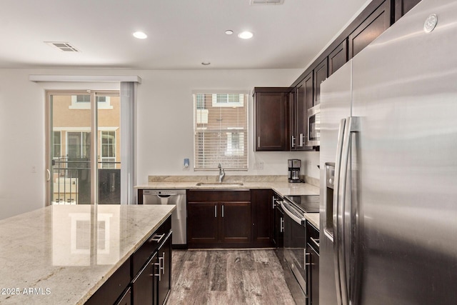 kitchen featuring light stone countertops, a sink, stainless steel appliances, wood finished floors, and visible vents