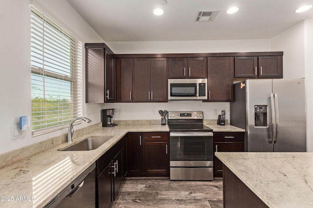 kitchen featuring dark brown cabinets, light stone countertops, a sink, dark wood finished floors, and stainless steel appliances