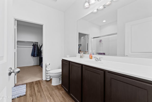 bathroom featuring a spacious closet, toilet, a shower with shower door, vanity, and wood finished floors