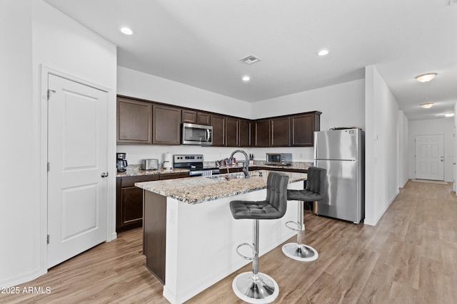 kitchen with visible vents, light stone counters, appliances with stainless steel finishes, dark brown cabinets, and a sink