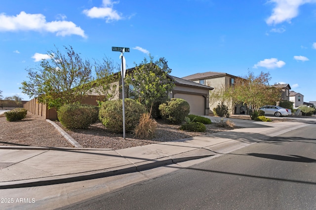 view of property hidden behind natural elements featuring an attached garage, concrete driveway, and stucco siding