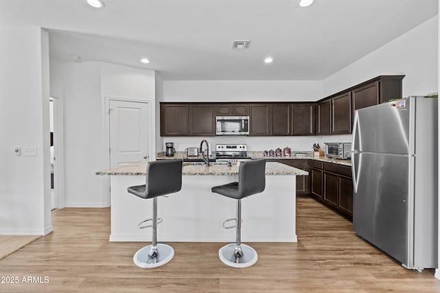 kitchen with an island with sink, dark brown cabinetry, visible vents, and stainless steel appliances