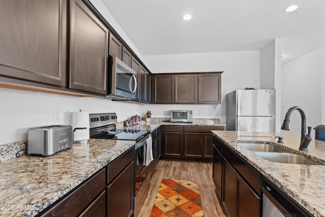 kitchen featuring a sink, dark brown cabinets, appliances with stainless steel finishes, light wood-type flooring, and light stone countertops