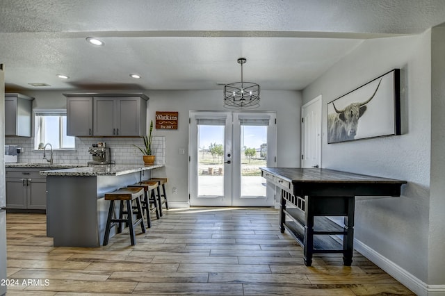 kitchen with pendant lighting, french doors, gray cabinets, light stone countertops, and light hardwood / wood-style floors