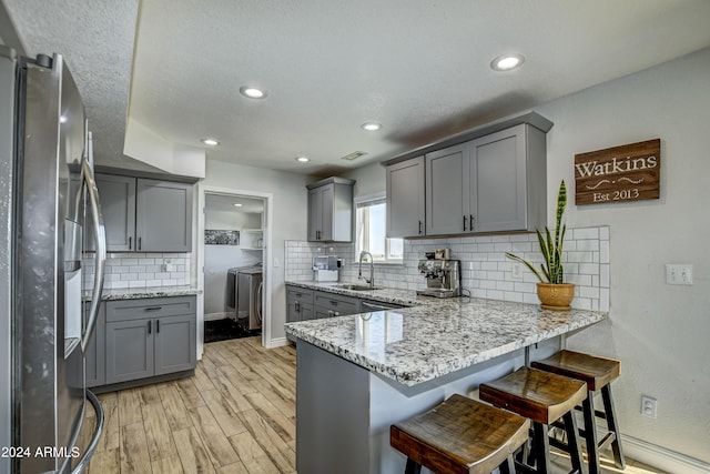 kitchen featuring gray cabinetry, sink, kitchen peninsula, light hardwood / wood-style flooring, and stainless steel fridge with ice dispenser