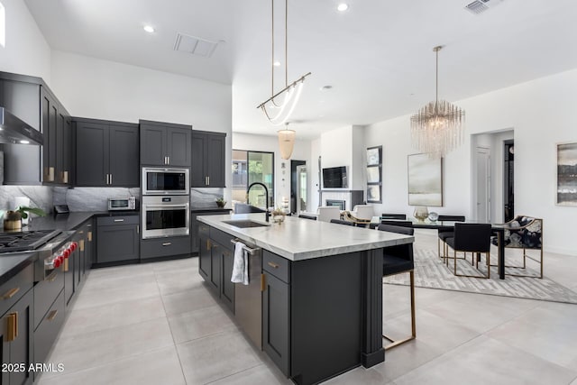 kitchen with a breakfast bar, pendant lighting, an island with sink, sink, and stainless steel appliances