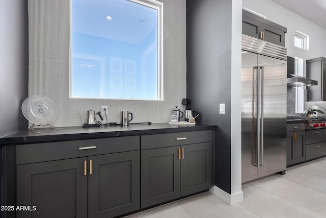 interior space featuring gray cabinetry, light tile patterned floors, built in fridge, and wall chimney exhaust hood