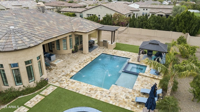 view of pool featuring a pool with connected hot tub, a patio, a fenced backyard, a gazebo, and exterior kitchen