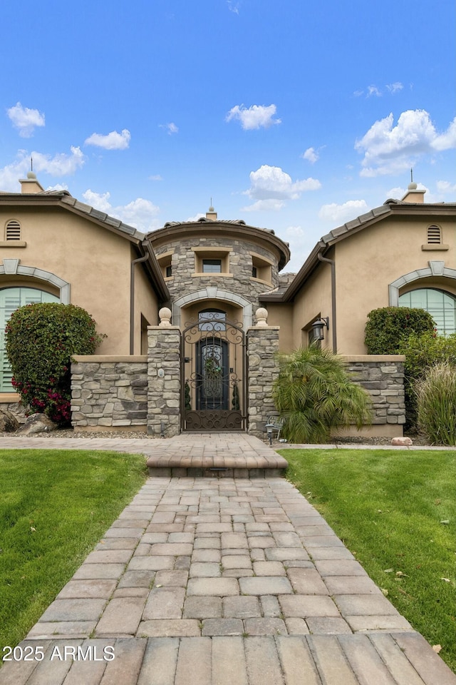 entrance to property with a gate, a lawn, stone siding, and stucco siding