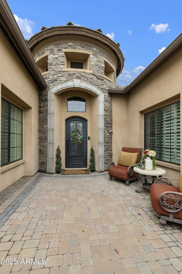 doorway to property with a patio, stone siding, and stucco siding