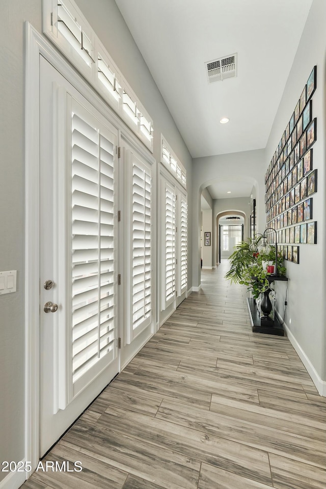 hallway with visible vents, arched walkways, baseboards, and light wood-style flooring