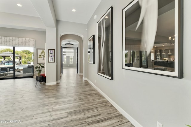 corridor with recessed lighting, wood finished floors, baseboards, and arched walkways