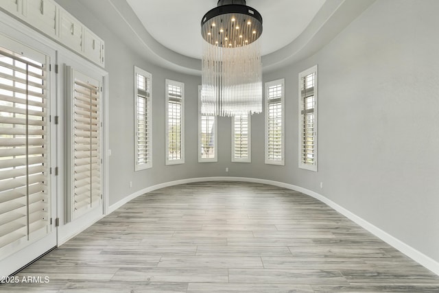 empty room with baseboards, an inviting chandelier, and light wood finished floors