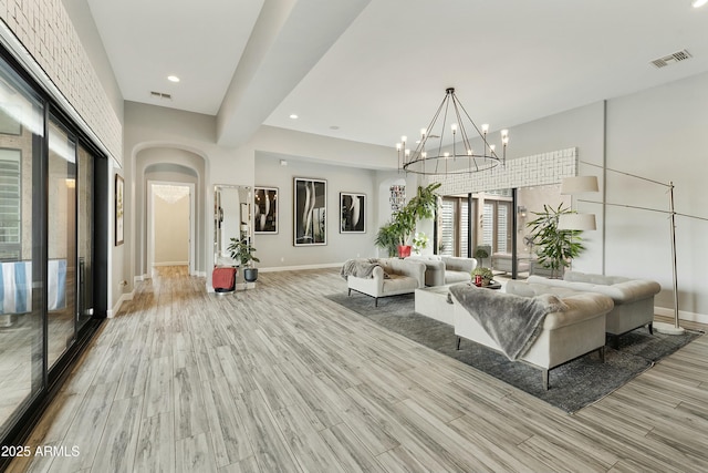 living area featuring arched walkways, visible vents, an inviting chandelier, and wood finished floors