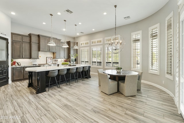 kitchen featuring light countertops, an island with sink, visible vents, and backsplash