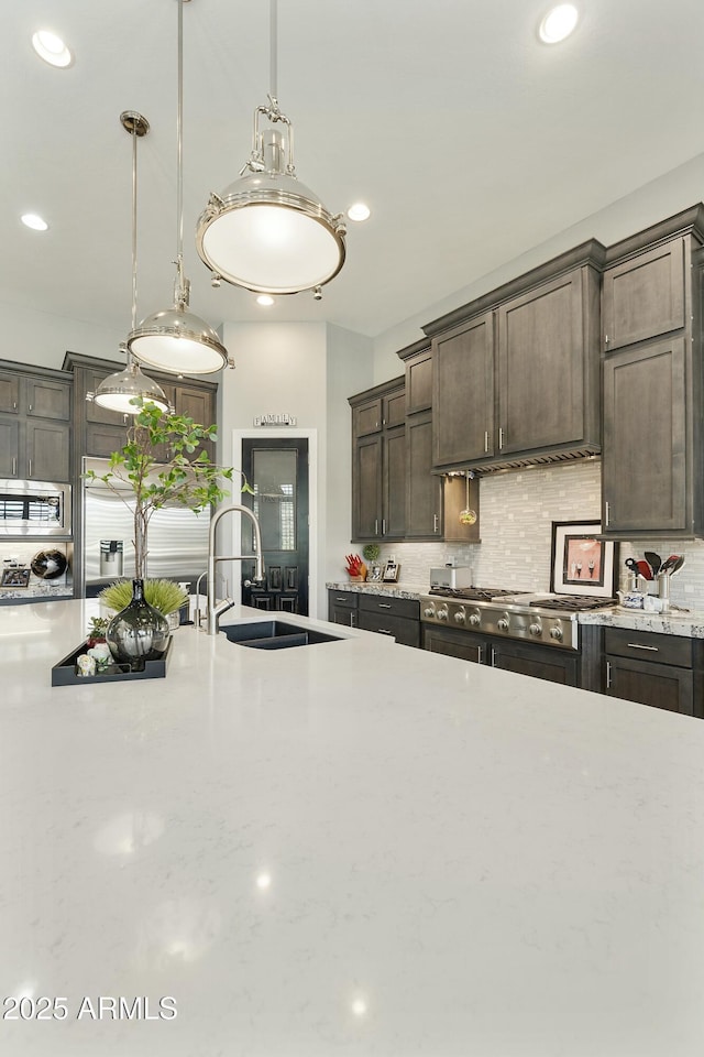 kitchen with hanging light fixtures, dark brown cabinets, tasteful backsplash, and a sink