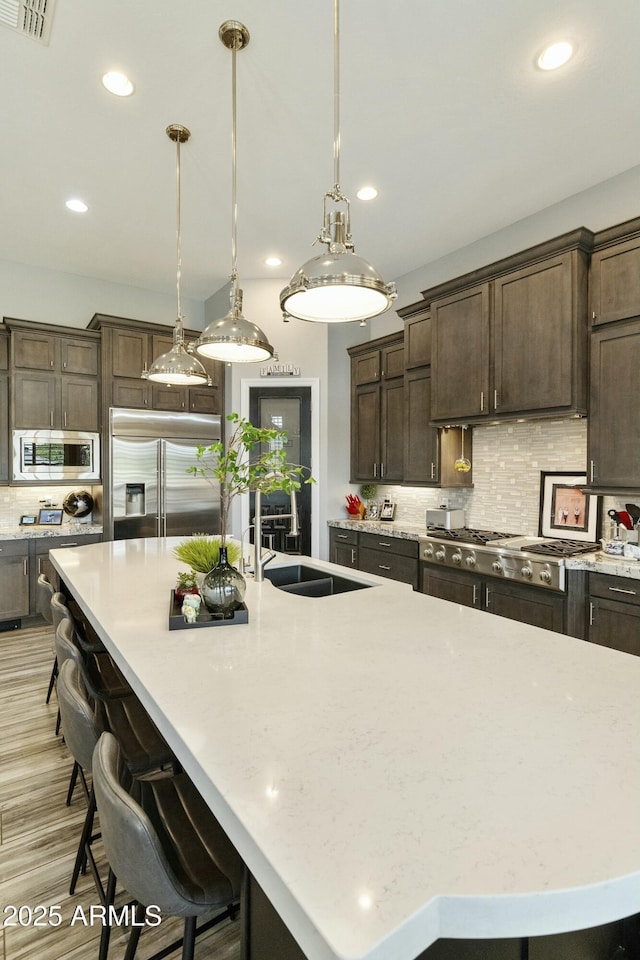 kitchen featuring a large island with sink, a sink, dark brown cabinetry, built in appliances, and backsplash