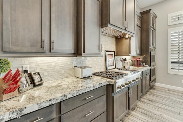 kitchen featuring light stone countertops, baseboards, stainless steel gas cooktop, dark brown cabinetry, and backsplash