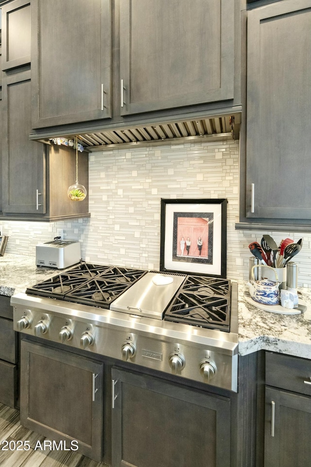 kitchen with light stone counters, decorative backsplash, and stainless steel gas stovetop