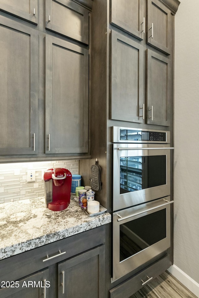 kitchen featuring light stone counters, wood finished floors, baseboards, stainless steel double oven, and decorative backsplash