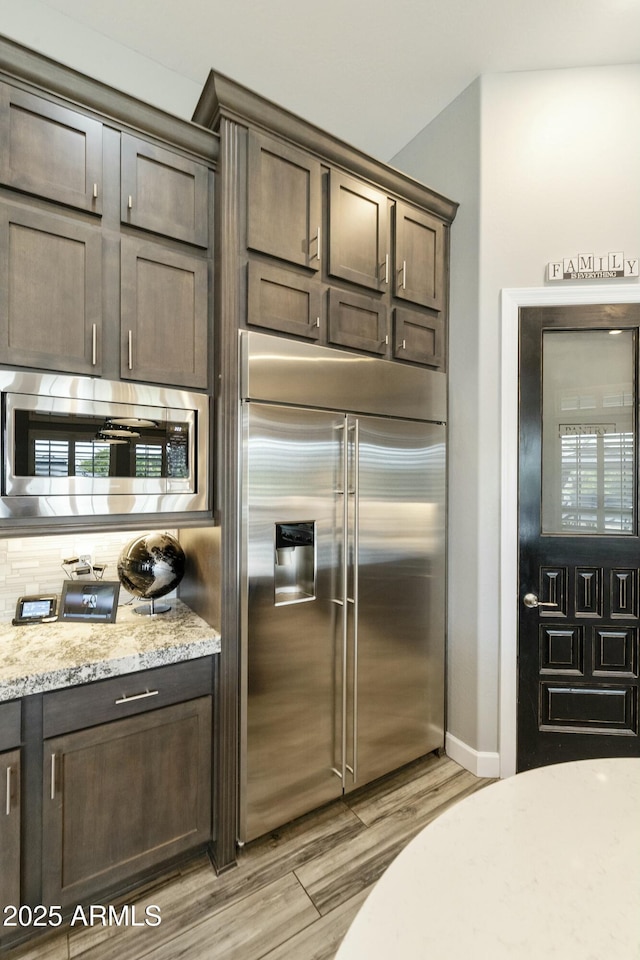 kitchen with light wood finished floors, light stone counters, dark brown cabinets, and built in appliances