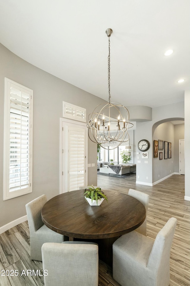 dining area with baseboards, arched walkways, an inviting chandelier, and wood finished floors