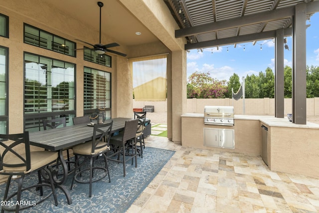 view of patio with area for grilling, a ceiling fan, fence, outdoor dining area, and an outdoor kitchen