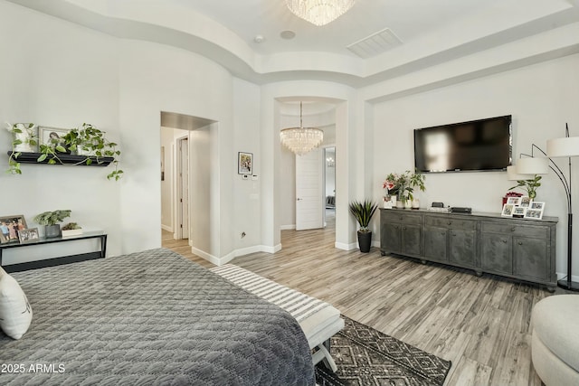 bedroom with visible vents, arched walkways, an inviting chandelier, light wood finished floors, and baseboards