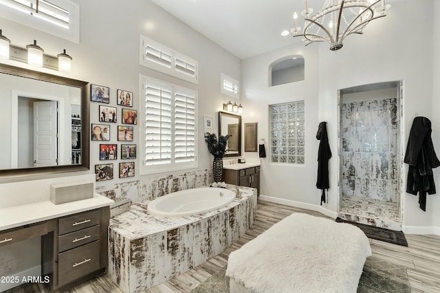 full bathroom featuring wood finished floors, an inviting chandelier, tiled shower, a bath, and vanity