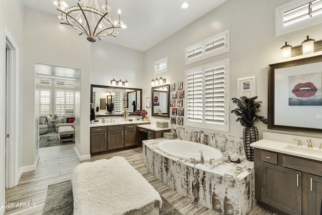 bathroom featuring a garden tub, a notable chandelier, two vanities, and a sink