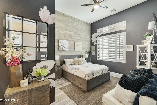 bedroom with visible vents, an accent wall, baseboards, wood finished floors, and a ceiling fan