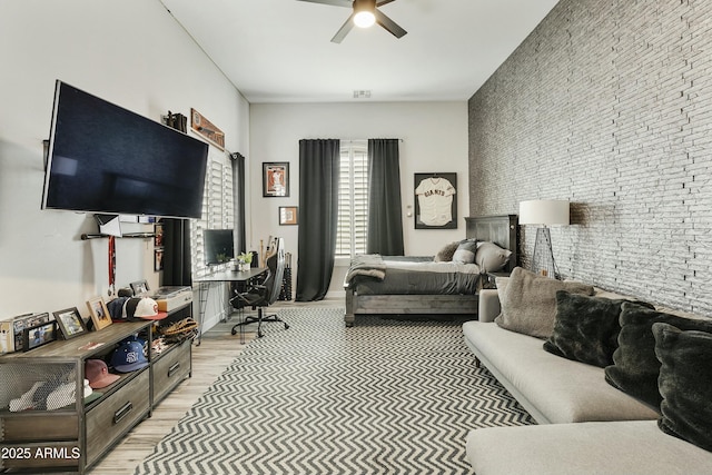 bedroom featuring light wood finished floors, visible vents, an accent wall, and a ceiling fan