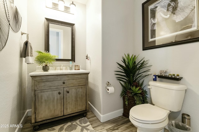 half bathroom featuring baseboards, toilet, wood finished floors, and vanity