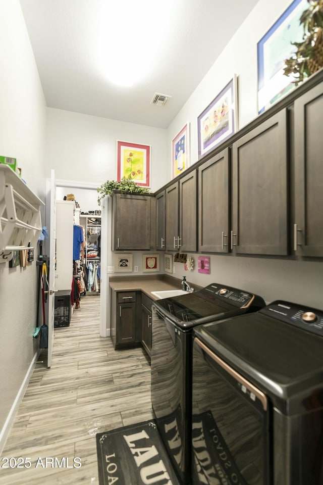 clothes washing area featuring visible vents, cabinet space, a sink, light wood-type flooring, and washer and clothes dryer