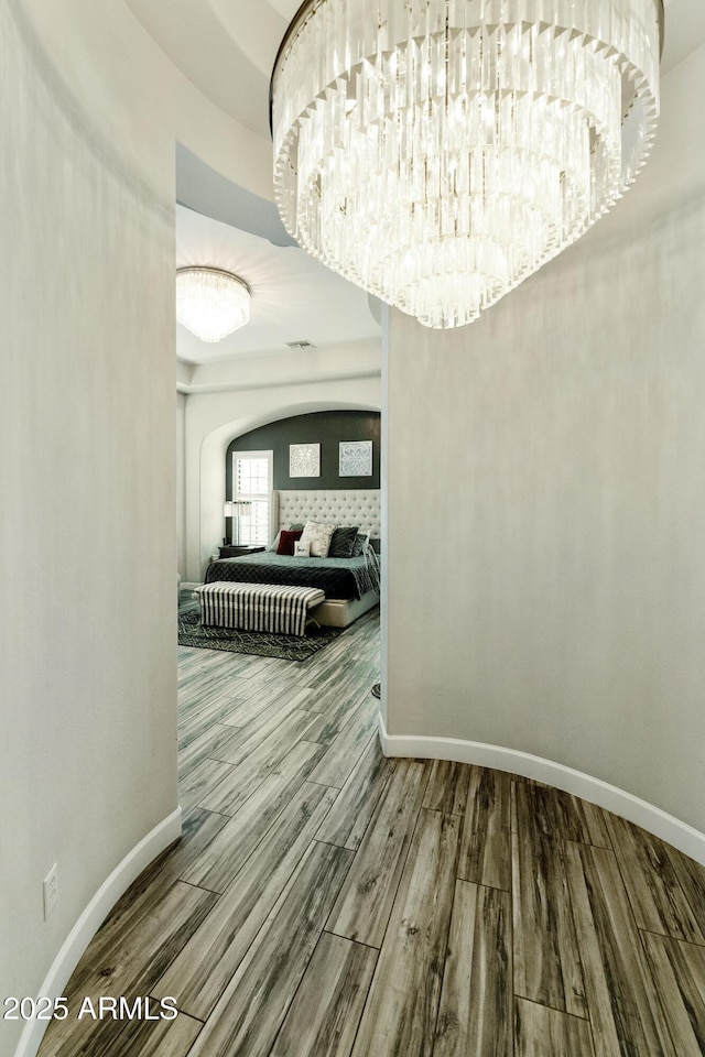 hallway with visible vents, wood finished floors, arched walkways, and baseboards