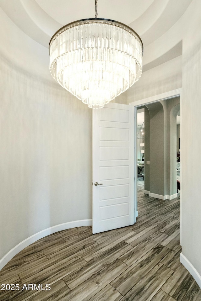 empty room featuring baseboards, wood finished floors, and a chandelier