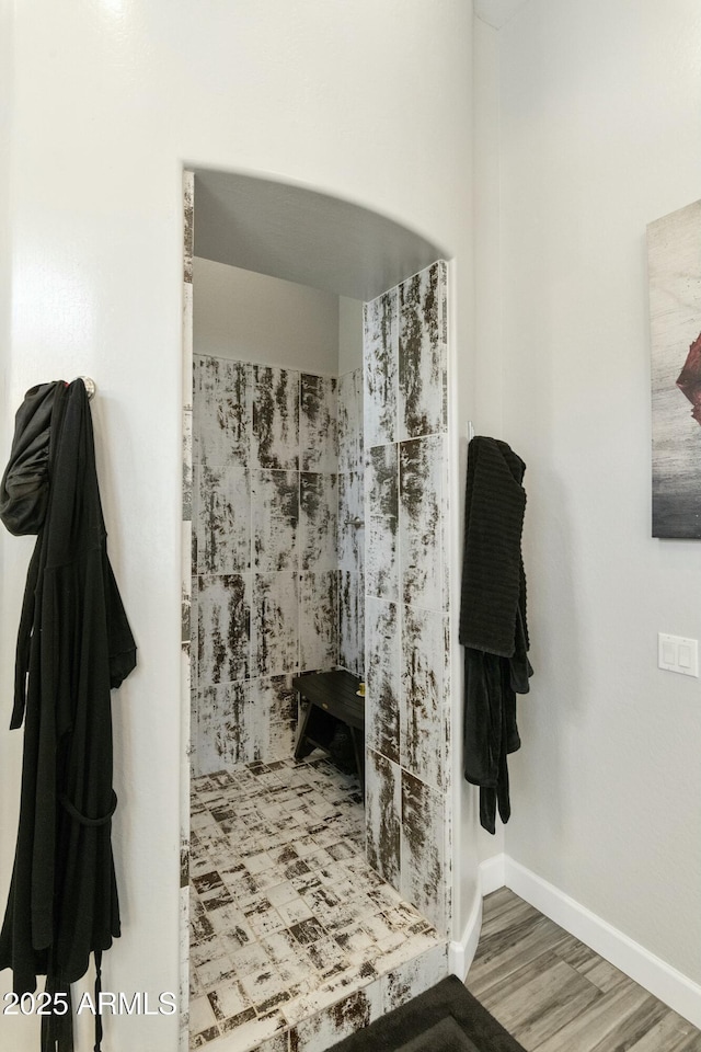 full bath featuring a tile shower, baseboards, and wood finished floors