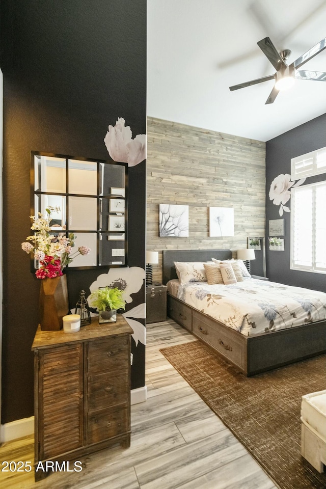 bedroom featuring light wood finished floors, wood walls, an accent wall, and a ceiling fan