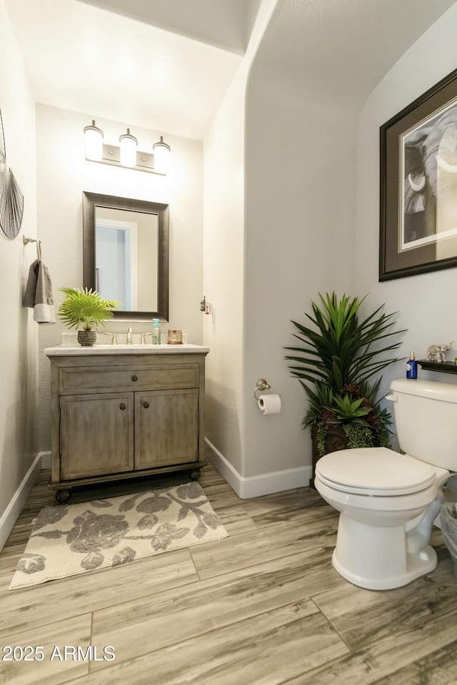 half bathroom with baseboards, toilet, wood finished floors, and vanity