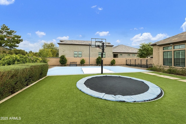 view of sport court with a trampoline, a lawn, and fence