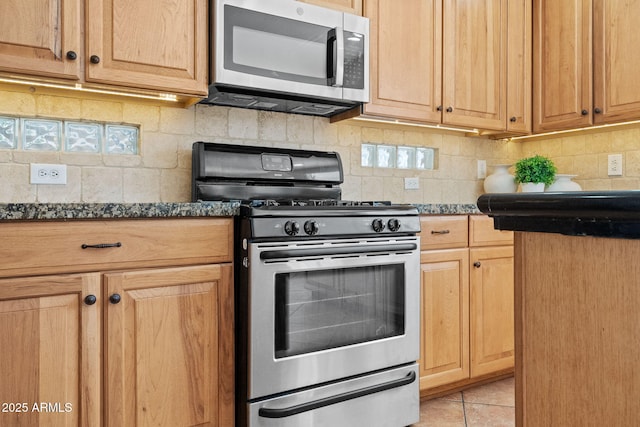 kitchen with dark stone counters, appliances with stainless steel finishes, light tile patterned flooring, and decorative backsplash