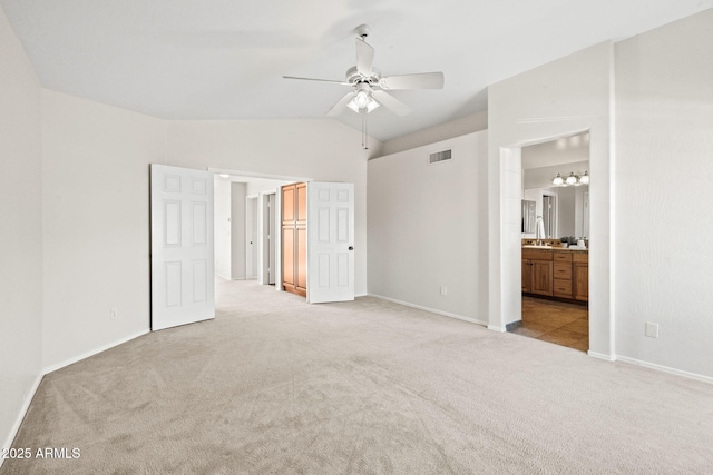 unfurnished bedroom with lofted ceiling, ensuite bathroom, ceiling fan, and light carpet