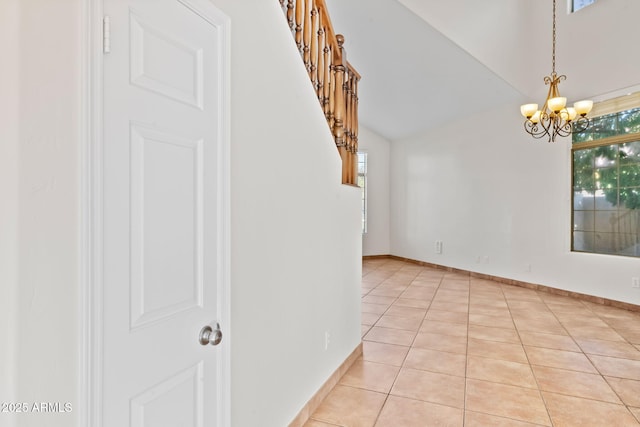 tiled empty room featuring lofted ceiling and a notable chandelier