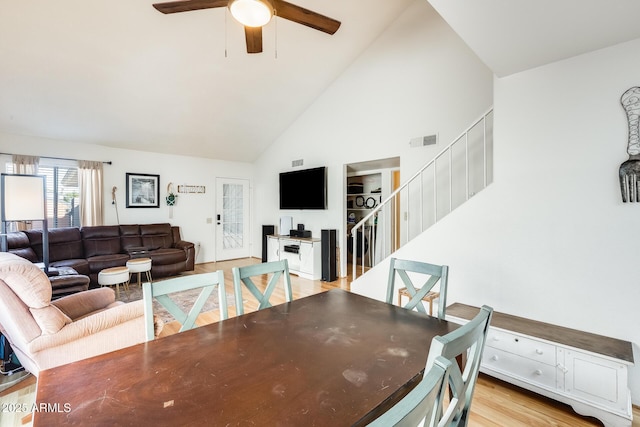 dining room with visible vents, ceiling fan, stairs, light wood-style floors, and high vaulted ceiling