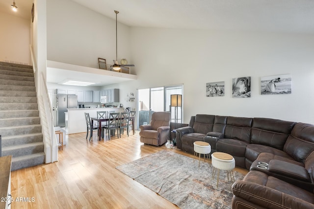 living room featuring high vaulted ceiling, light wood-type flooring, and stairs