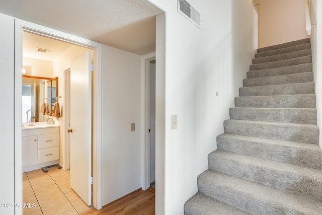 stairs featuring tile patterned flooring, visible vents, and a textured ceiling